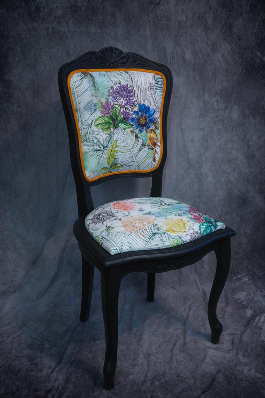 chaise peinte en noir avec du tissu à motifs
             de fleurs colorés, finition galon orangei